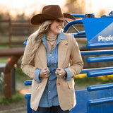 Woman in a beige western blazer and cowboy hat standing next to a blue piece of a priefert chute